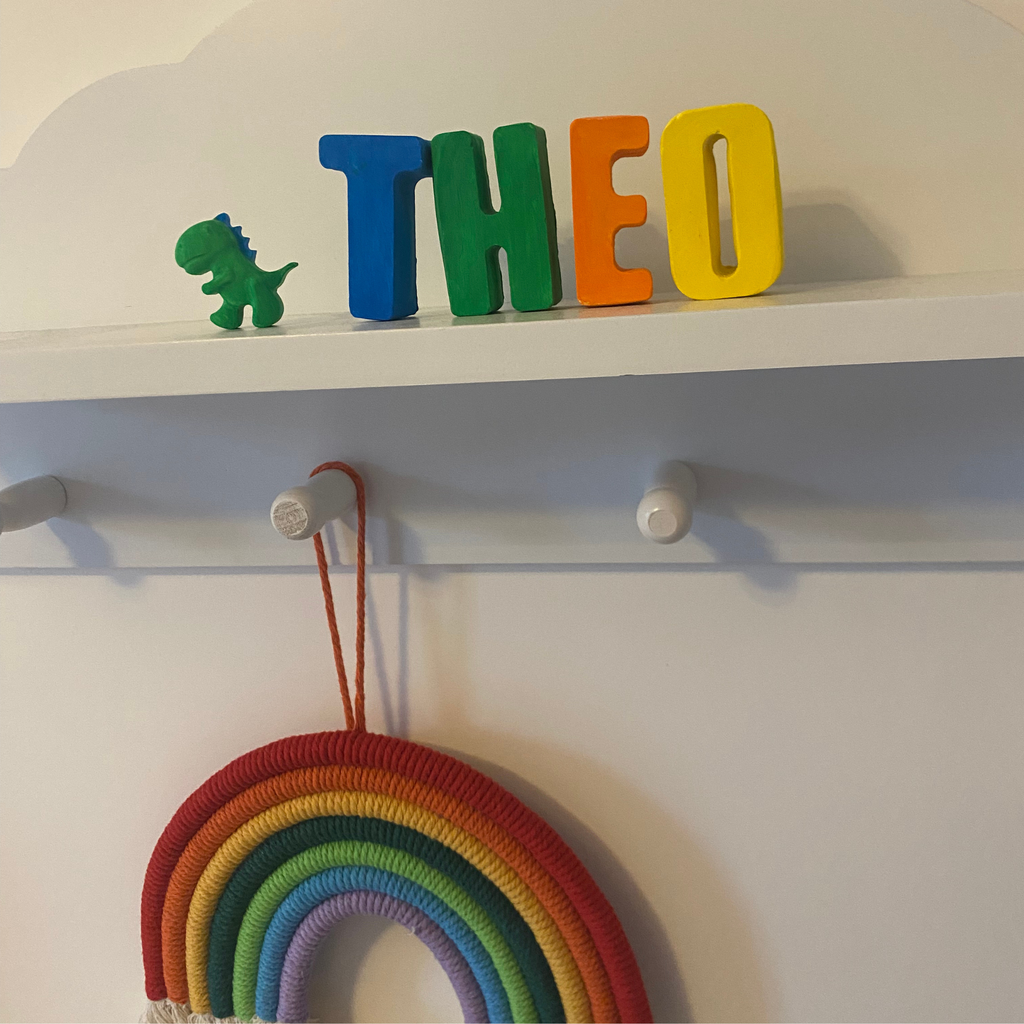 Colorful letters spelling 'THEO' above a rainbow decoration on a shelf.